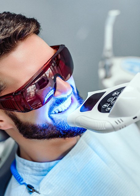 Man in protective glasses with UV light applied to teeth whitening