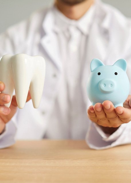 Dentist in white coat holding large model tooth and blue piggy bank