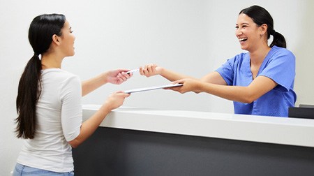 Smiling dental assistant handing patient form