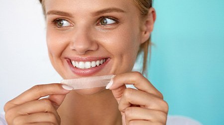 Woman placing whitening strip over upper arch