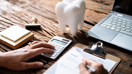 Hands at desk calculating invoice near large model tooth, stamp, and laptop