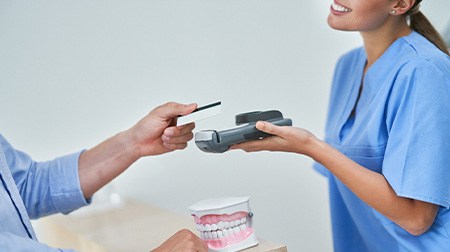 Woman holding out card reader to accept man’s payment at counter with model teeth
