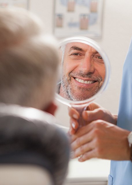 Man smiling at reflection in handheld mirror