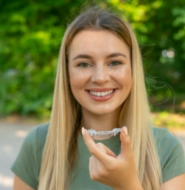 Smiling blonde woman holding an Invisalign clear aligner