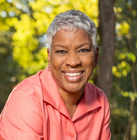 Older woman in peach colored blouse smiling outdoors