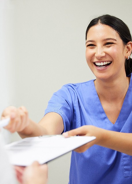 a dental assistant handing a patient new patient forms on a clipboard 