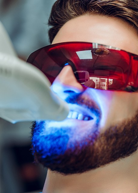 Woman in white shirt smiling into mirror with dentist’s gloved hands touching corners of her mouth