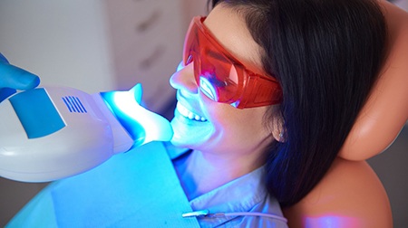Woman in dental chair with UV light shining on her smile